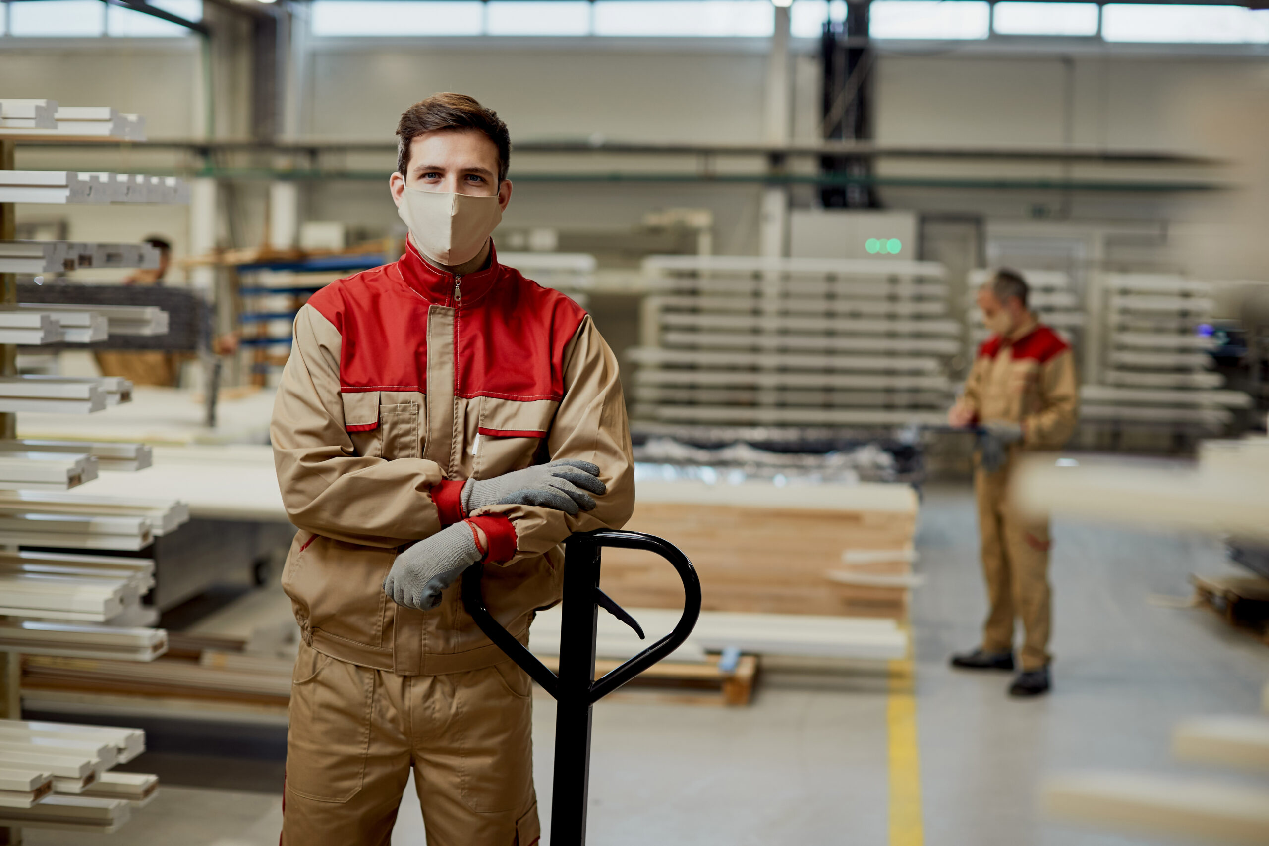 Portrait of male worker with protective face mask standing at carpentry workshop and looking at camera.